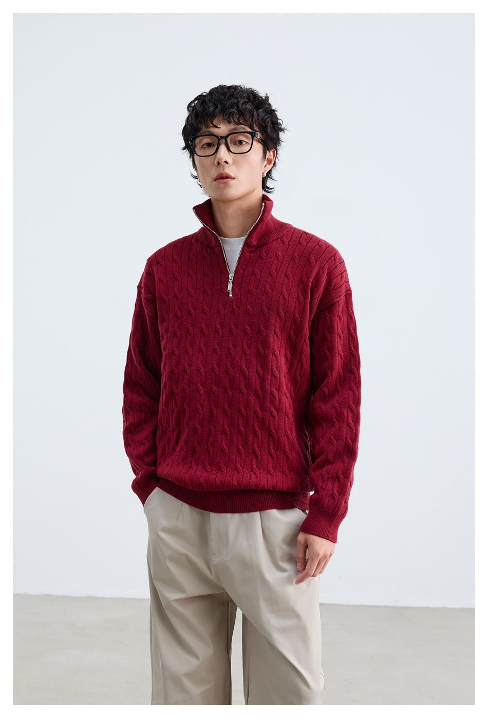 Model wearing a burgundy cable-knit quarter-zip sweater with beige trousers, shown from the front.