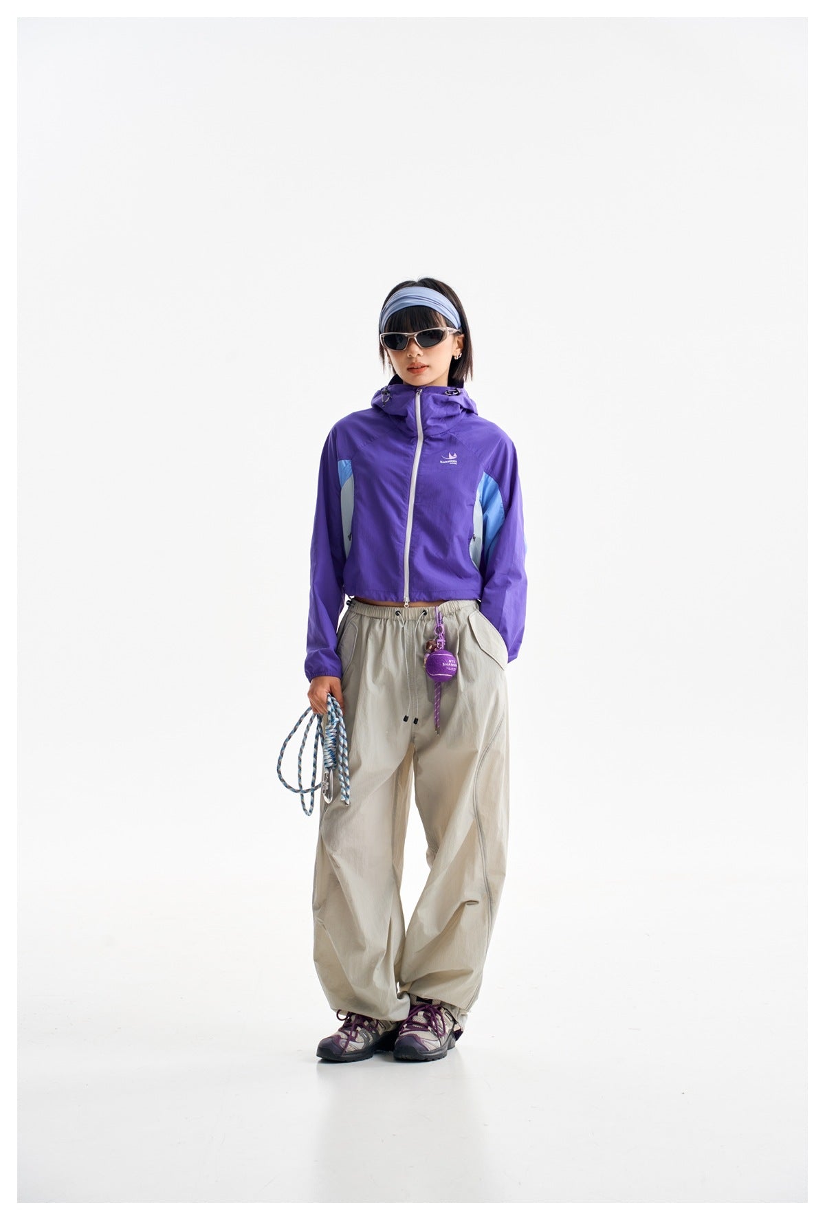 Model wearing a purple hooded jacket with light blue side panels and loose light gray pants.