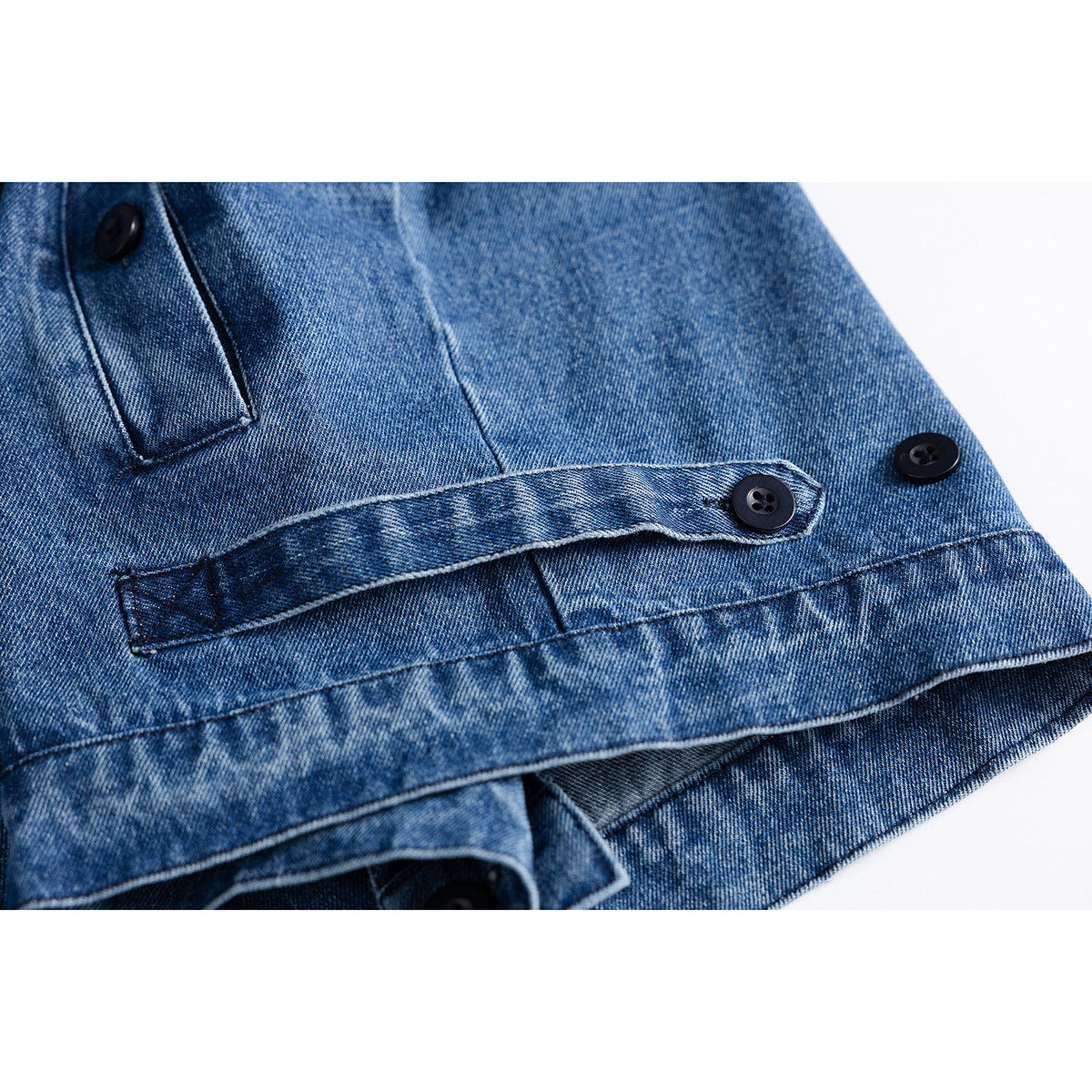 Close-up of a blue denim jacket hem with an adjustable button tab and dark buttons.