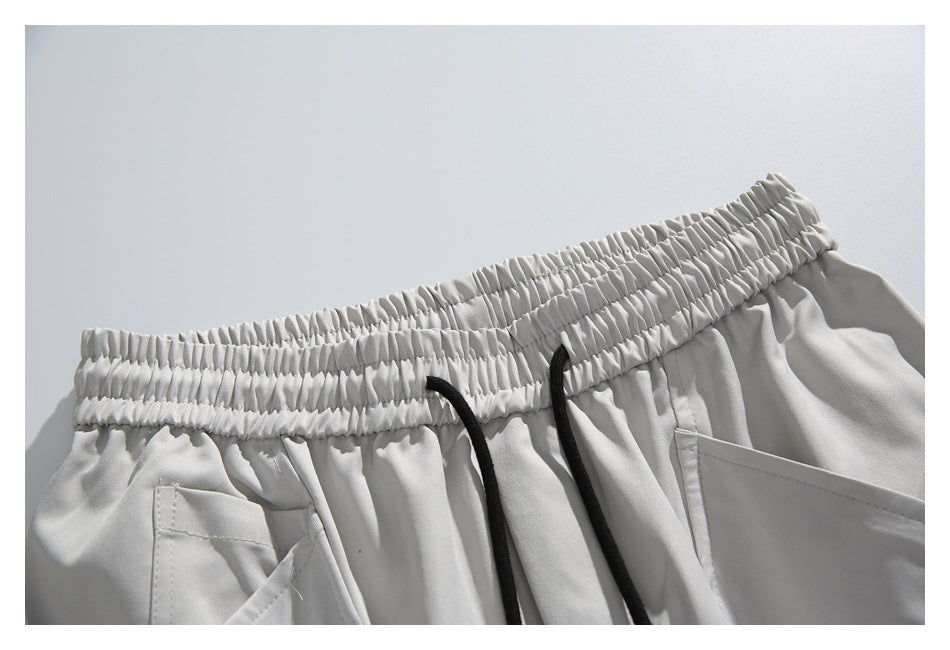 Close-up of light gray shorts with a gathered elastic waistband, black drawstrings, and front pockets.