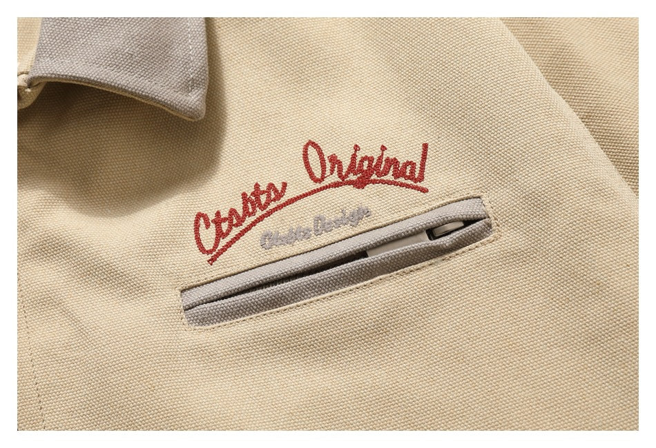 Close-up of a beige textured garment with red and gray embroidery above a narrow welt pocket with a zipper.
