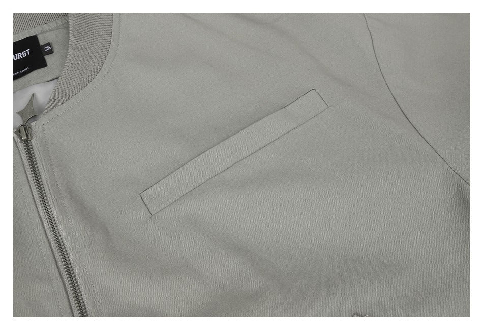 Close-up of the gray jacket's narrow welt chest pocket and front zipper edge.
