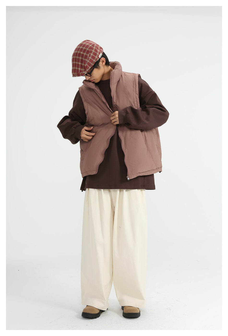 Model wearing dusty rose zip vest over a brown top with cream wide-leg pants, plaid flat cap and boots
