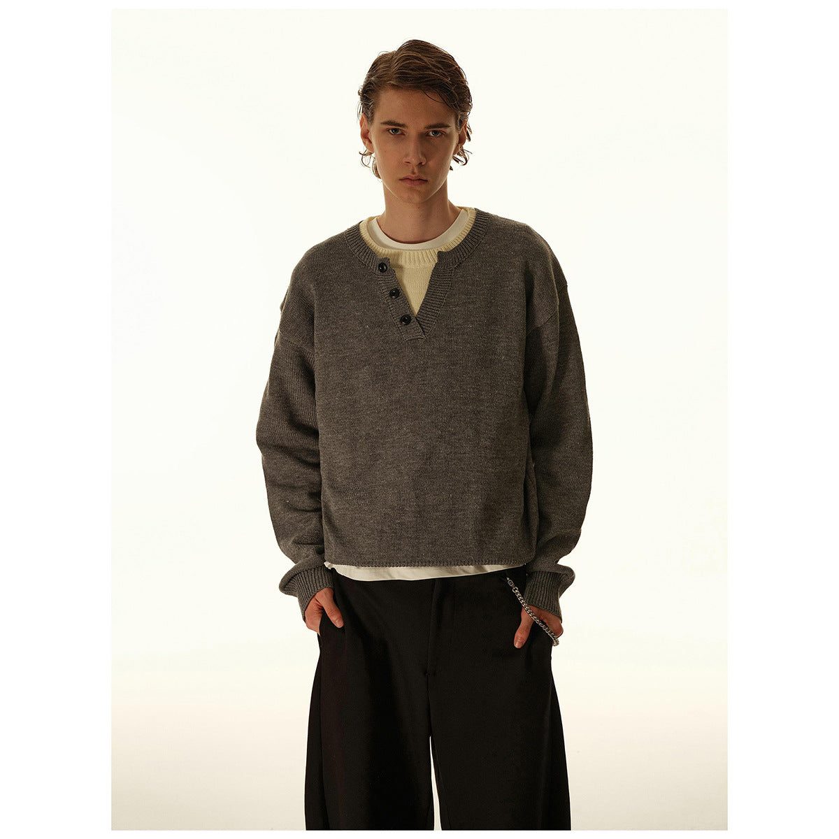 Man wearing a charcoal gray button-placket knit sweater over a cream shirt, shown from the front.