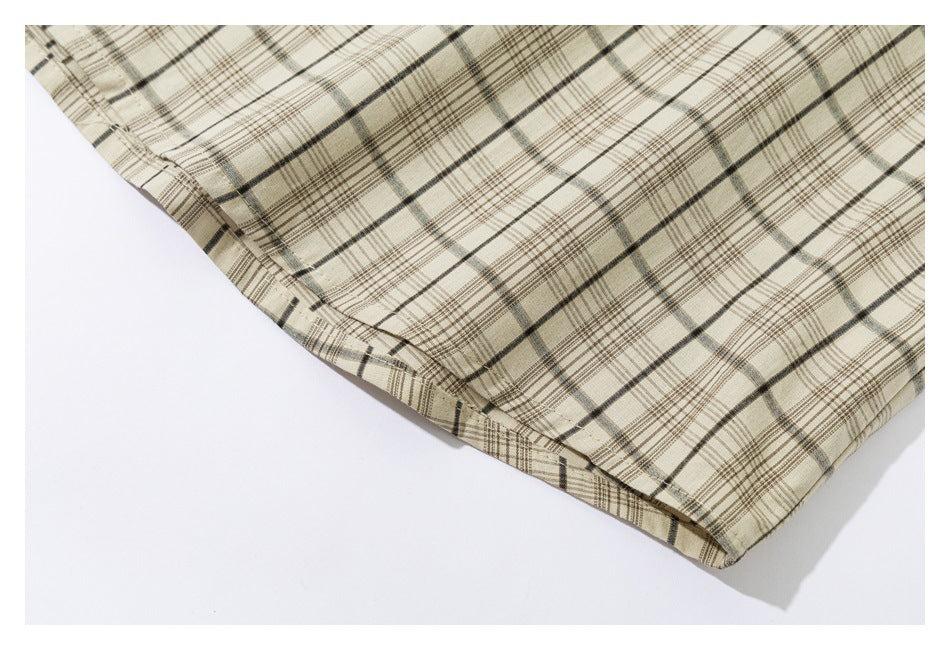 Close-up of the stitched hem on a beige plaid shirt laid flat.