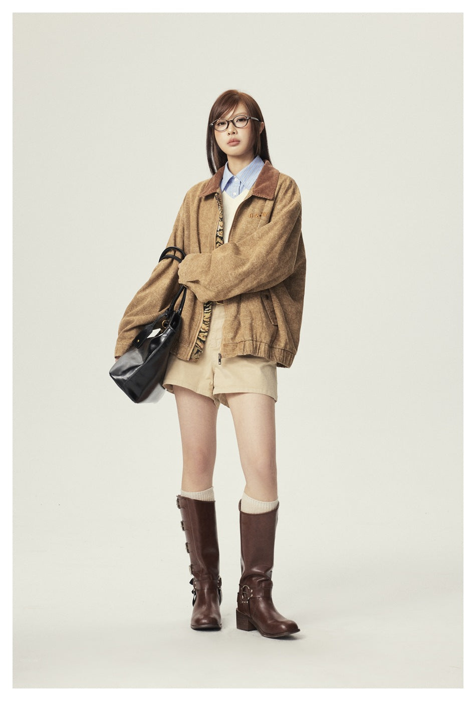 Full-length model view of a mottled tan jacket with a brown collar and zip front, styled with shorts and tall brown boots.