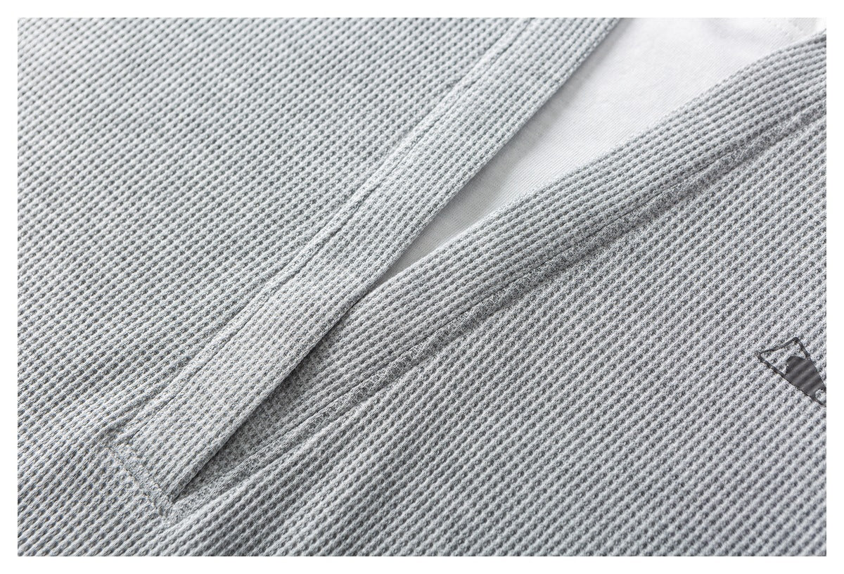 Close-up of a gray waffle-knit garment opening with a white inner panel and a small emblem.
