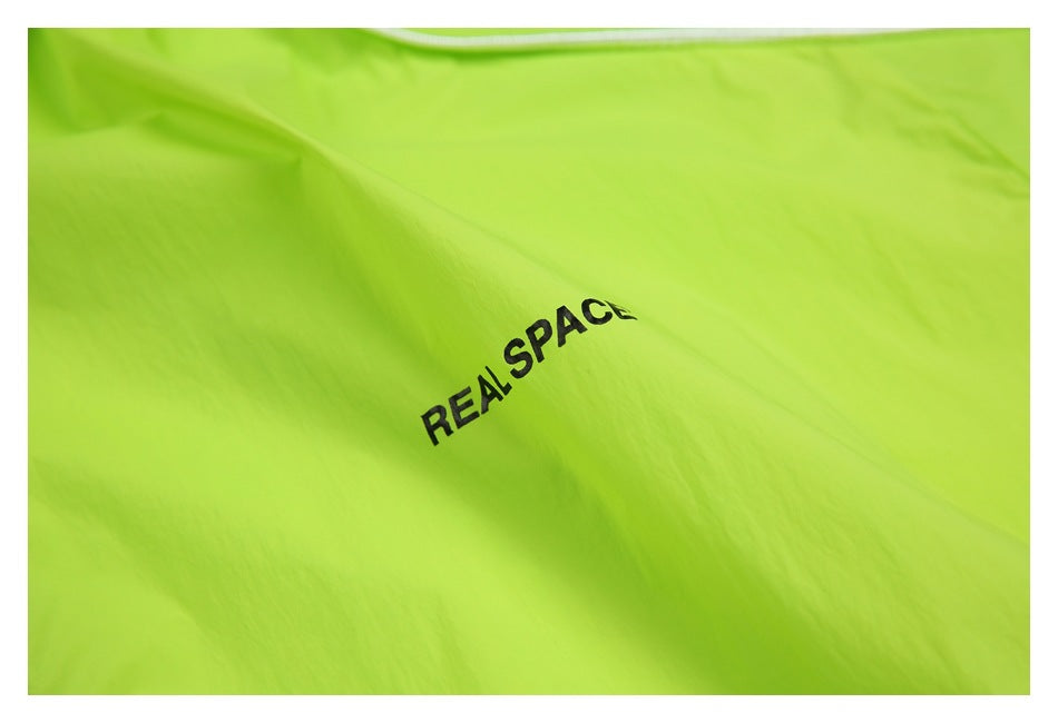Close-up of neon lime garment fabric with black REAL SPACE lettering.