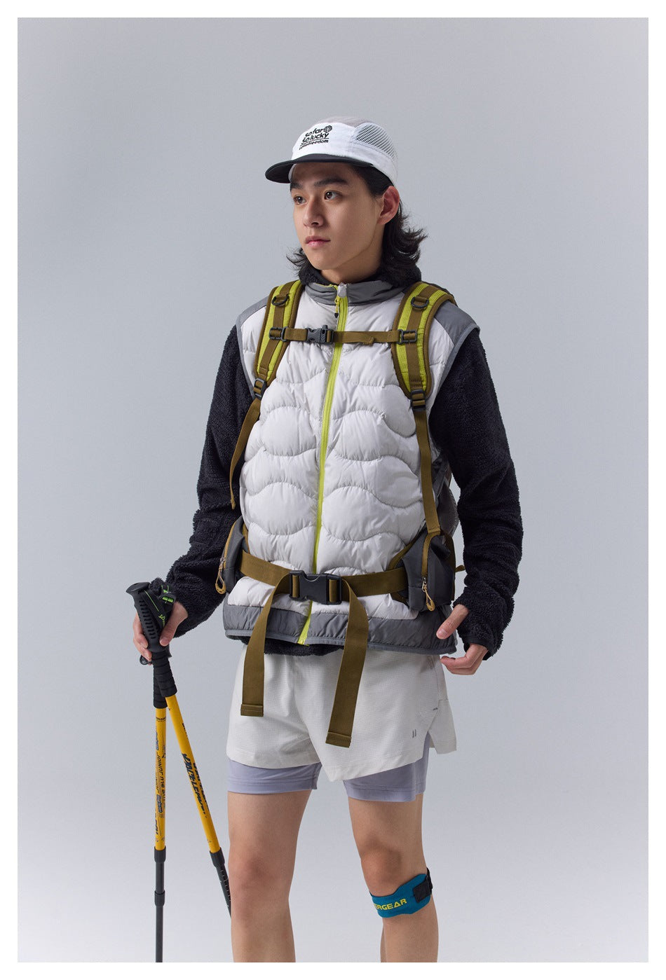Closer front view of a white quilted vest with gray panels and lime zipper trim, worn over a dark fleece top.