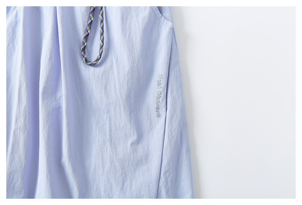 Close-up of pale lavender pants with a hanging patterned cord and small vertical lettering on the leg.