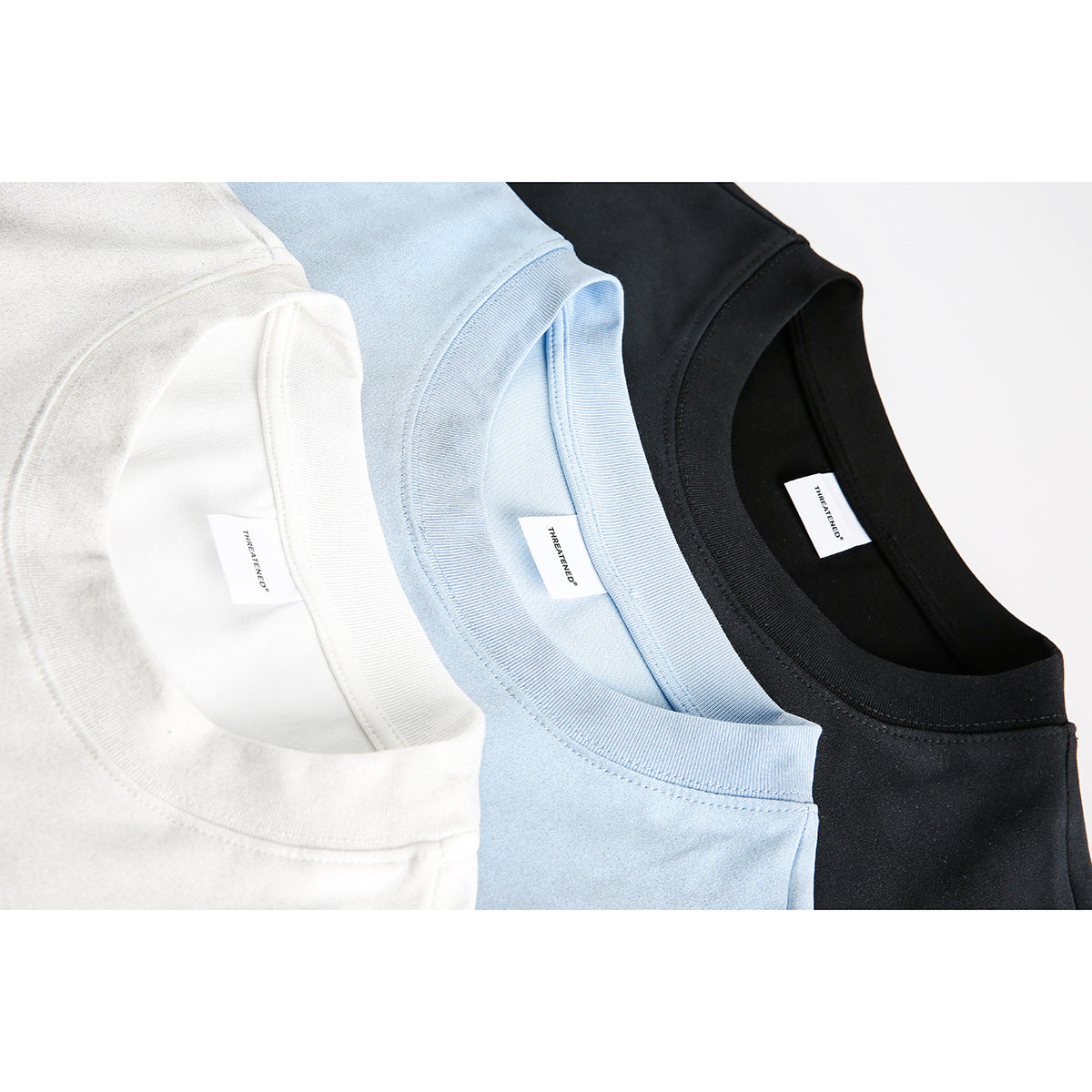 Close-up of white, pale blue, and black T-shirt crew necks with ribbed collars and inner labels.