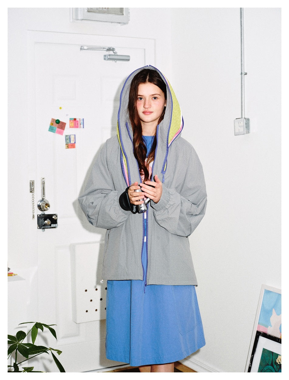 Model wearing a gray hooded jacket with blue, pink and lime hood trim, over a blue dress.