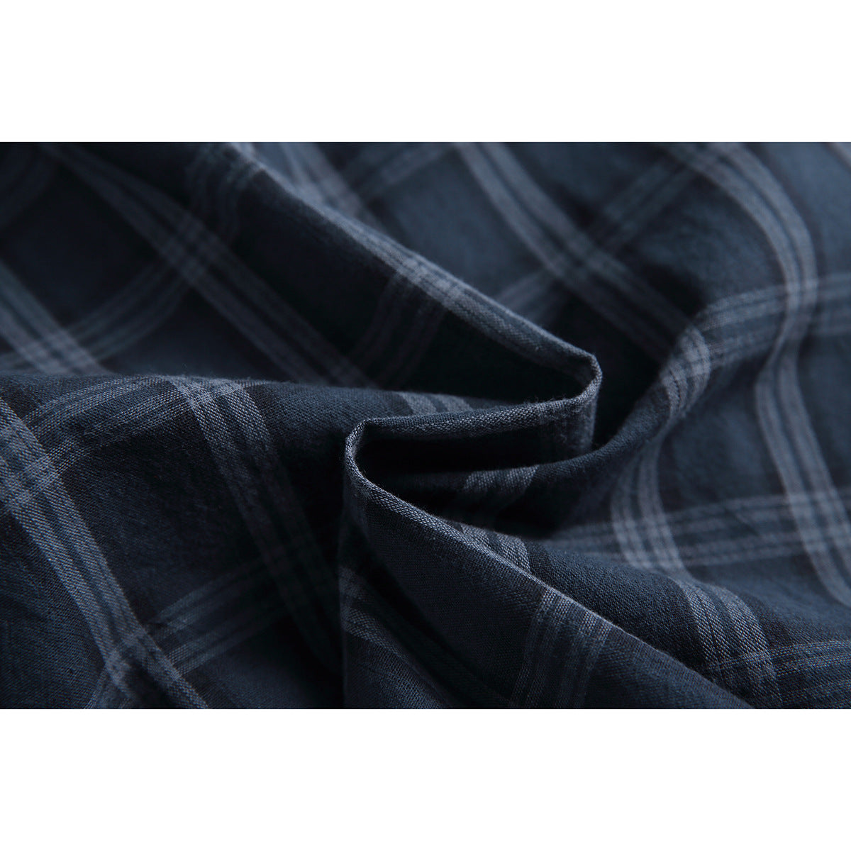 Close-up of dark navy plaid fabric arranged in folds, showing its woven texture and pattern.