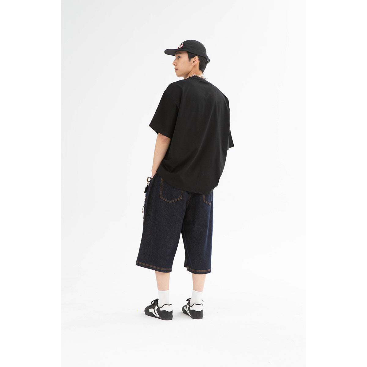 Rear view of a model wearing a plain black oversized T-shirt and dark indigo denim shorts.
