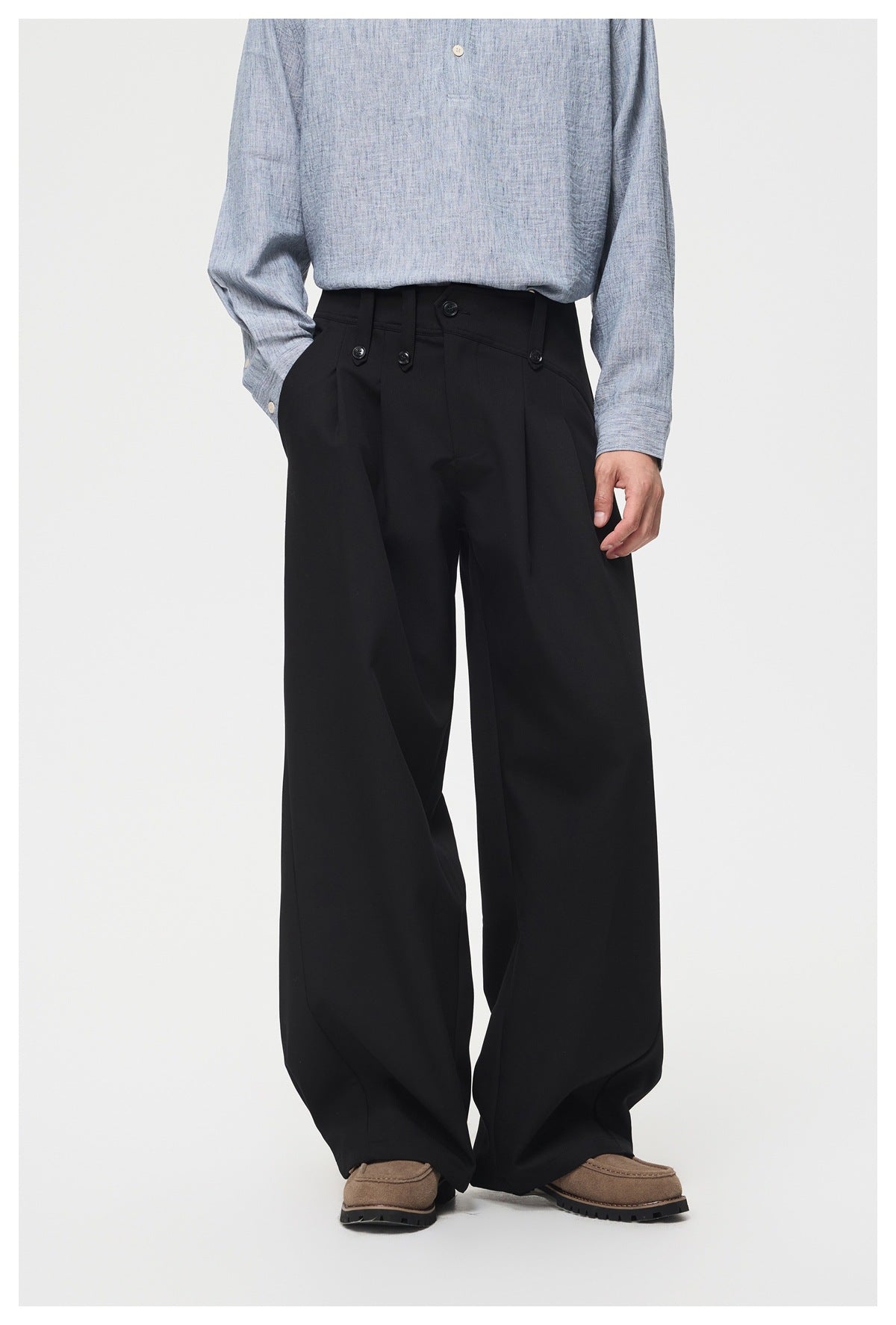 Front view of black wide-leg trousers worn by a model, with a high buttoned waistband and roomy legs.