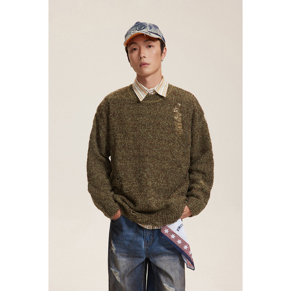 Model wearing an olive-brown marled crewneck sweater with distressed details over a striped shirt.