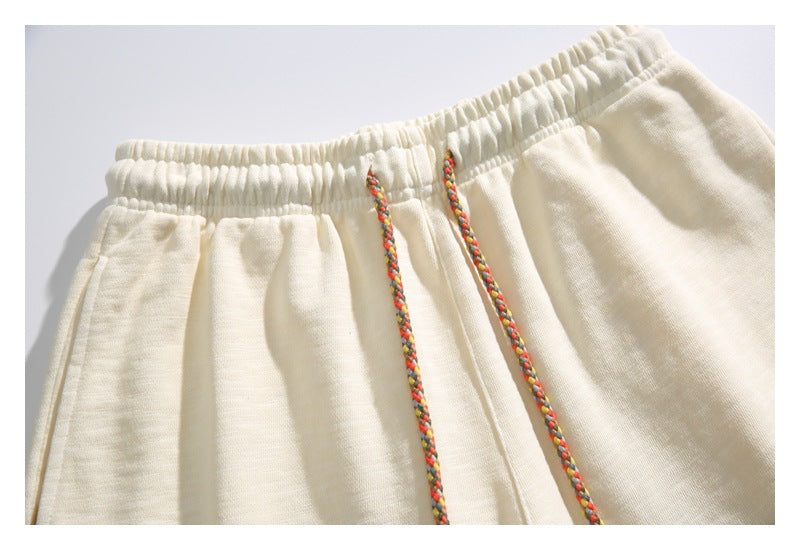 Close-up of the cream shorts' gathered elastic waistband and multicolored braided drawstrings.