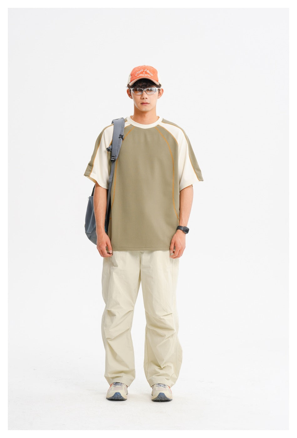 Model in green and cream raglan T-shirt with beige pants, orange cap, glasses and a gray shoulder bag, front view