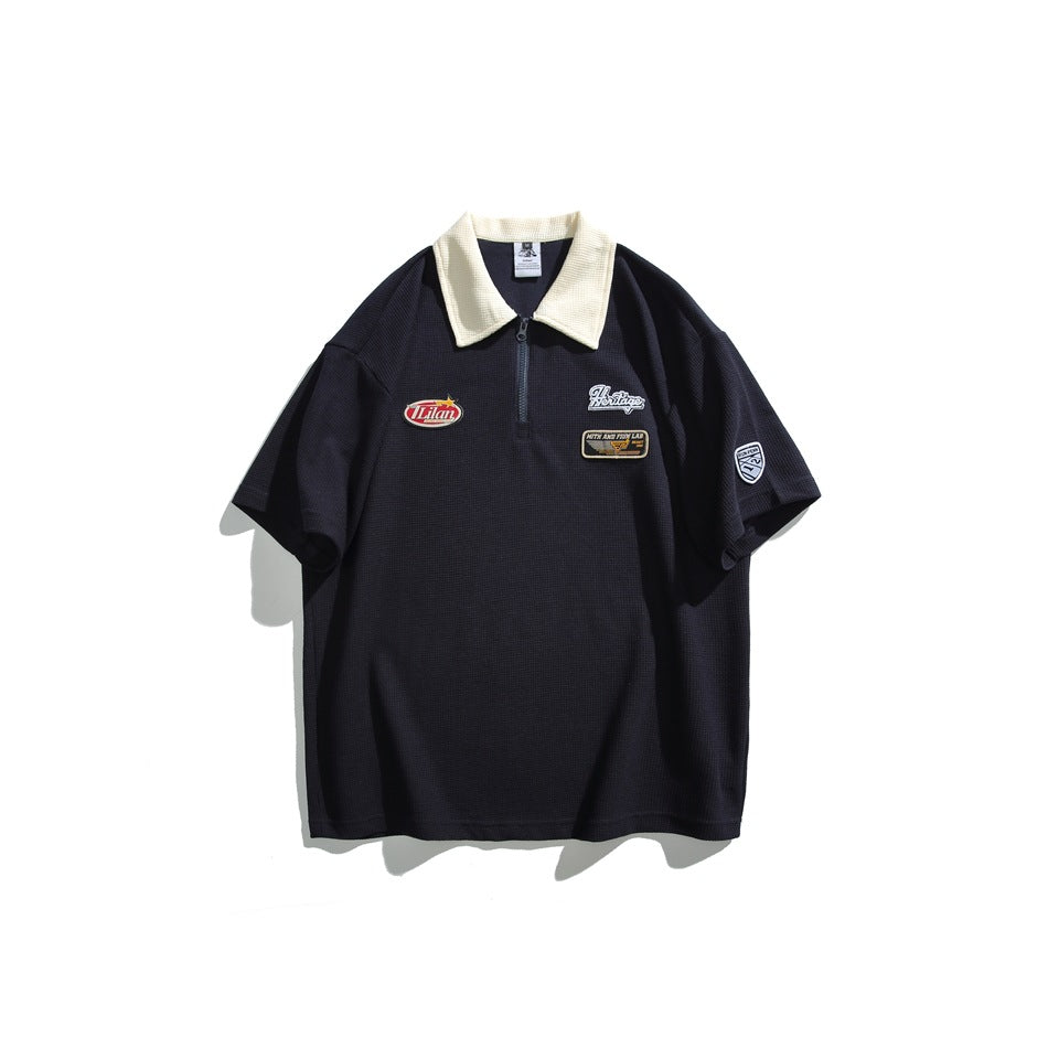 Navy waffle-knit short-sleeve polo with cream collar, quarter zipper and chest patches, flat front view