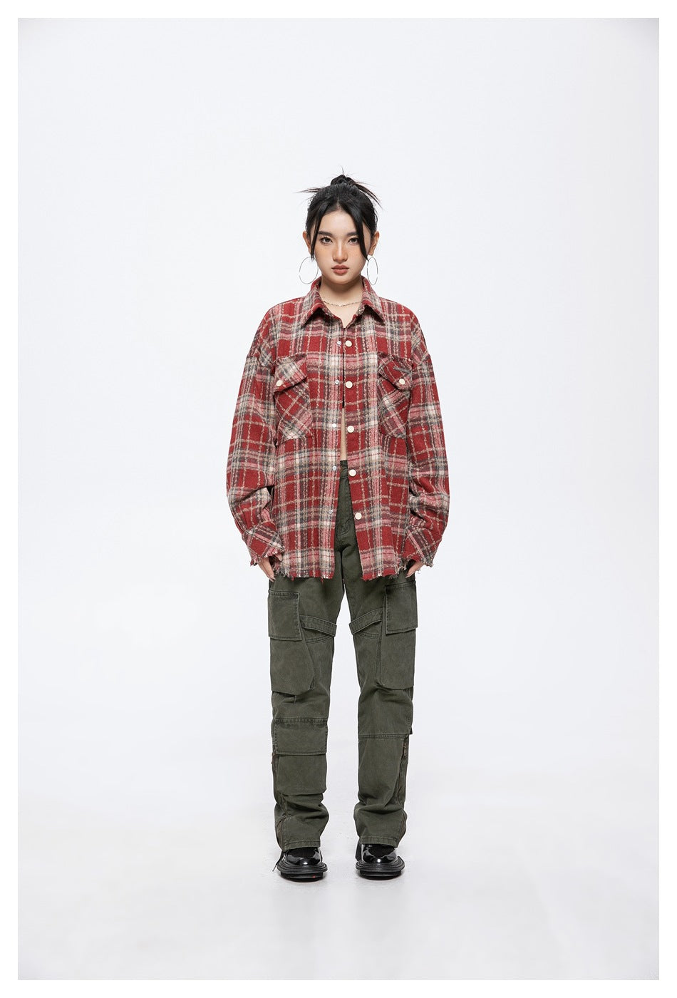 Front view of a model wearing an oversized red tartan button-up shirt jacket with flap pockets and frayed edges.