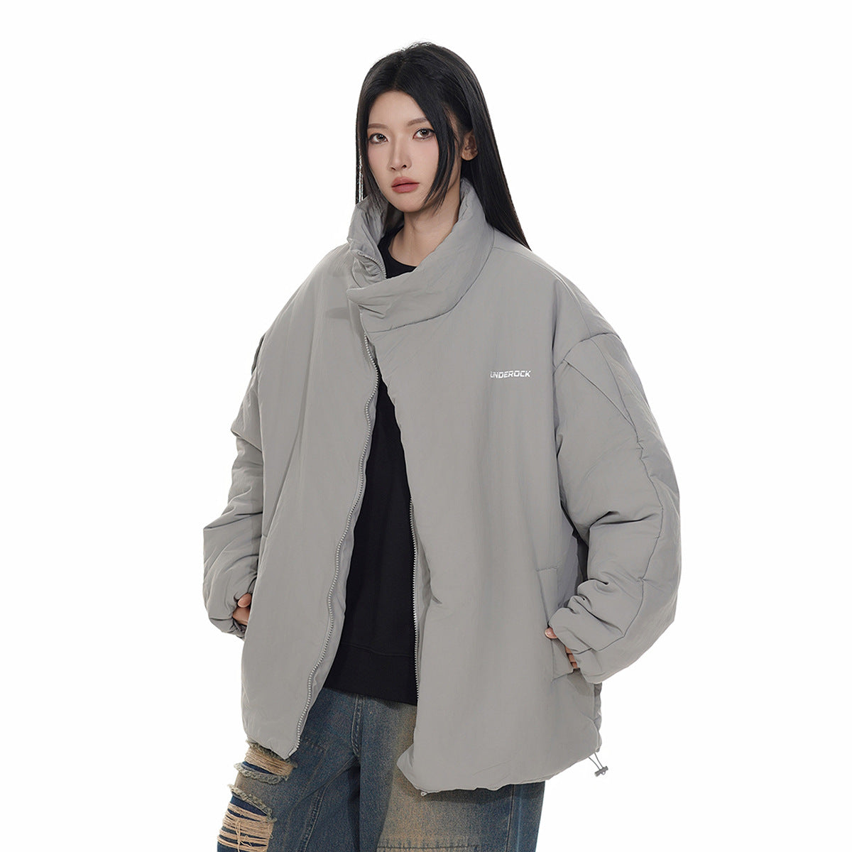 Model wearing an oversized light gray padded jacket with a tall folded collar and front zipper, paired with distressed jeans.