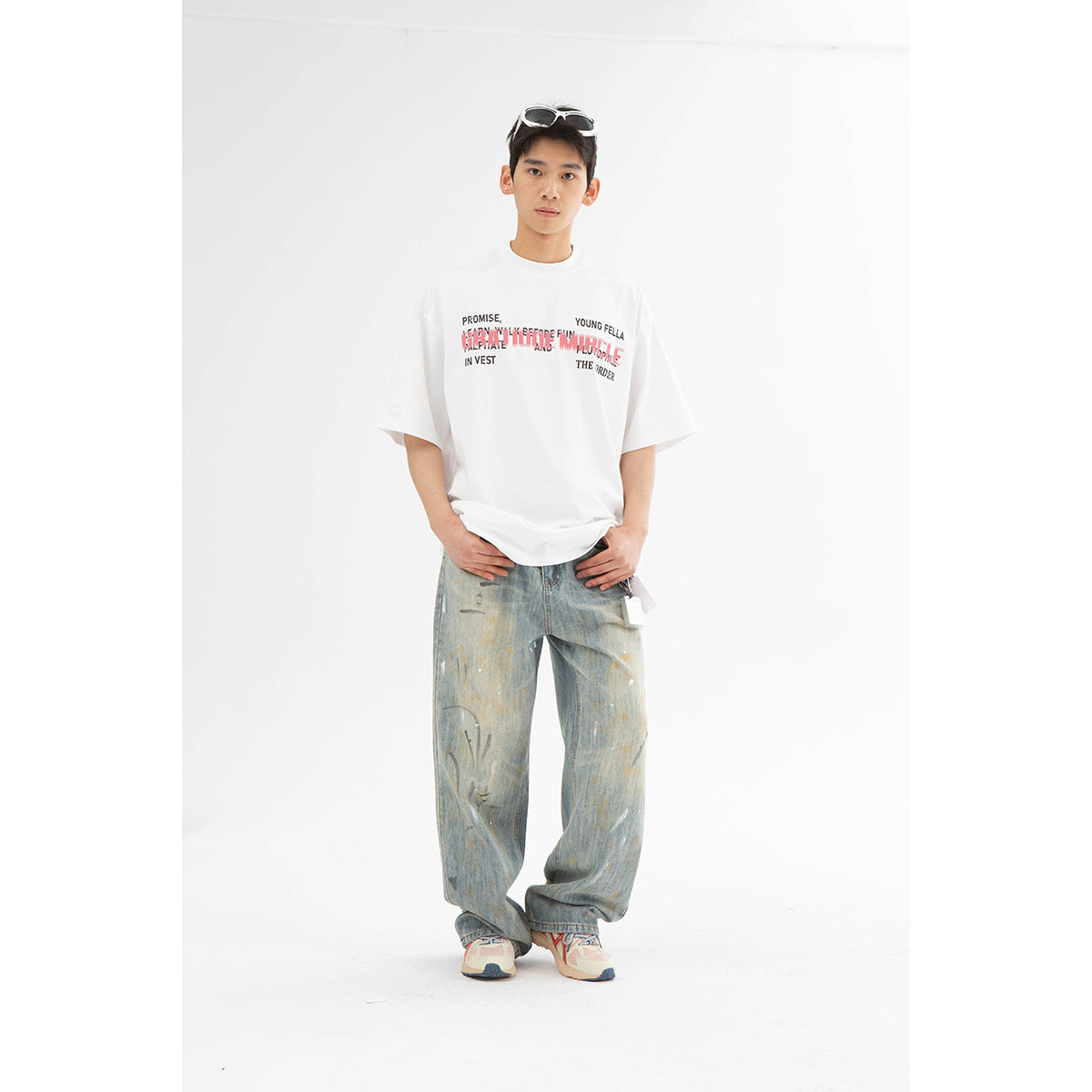 Model wearing an oversized white graphic T-shirt with distressed loose blue jeans and sneakers.