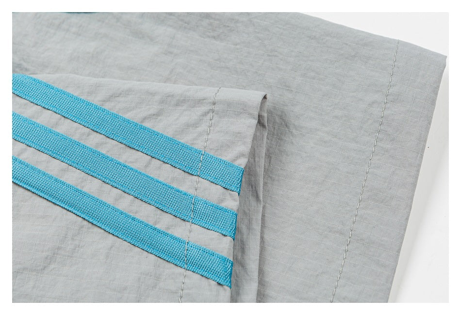 Close-up of three turquoise bands and stitching near the hem of light gray shorts.