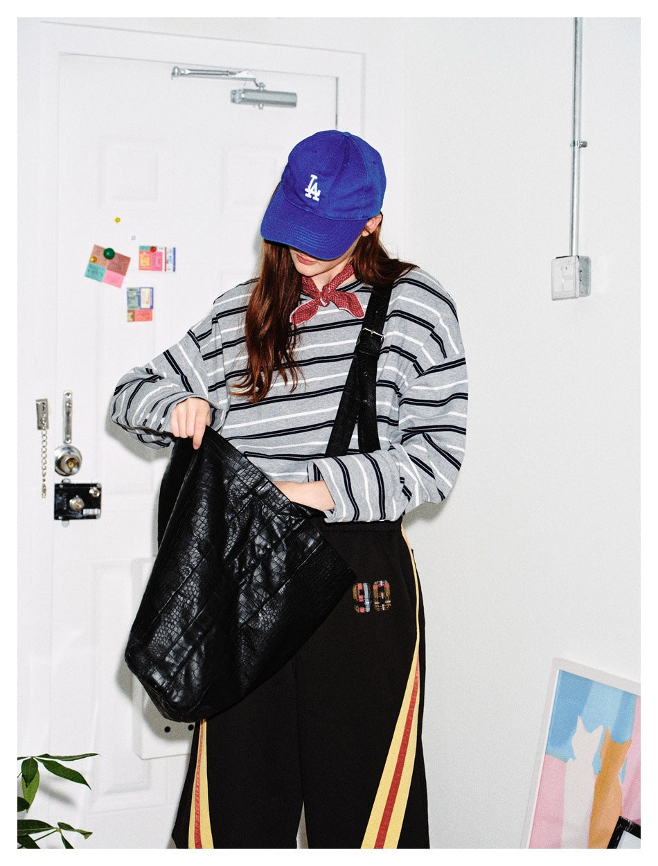 Person in gray striped long-sleeve top with blue cap, red bandana and black textured bag, face partly hidden