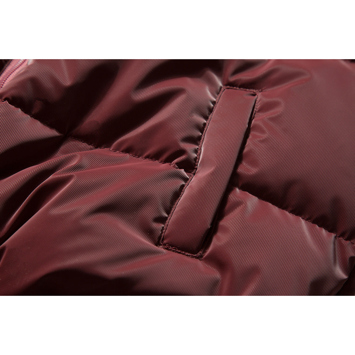 Close-up of burgundy quilted jacket fabric and a stitched vertical tab.