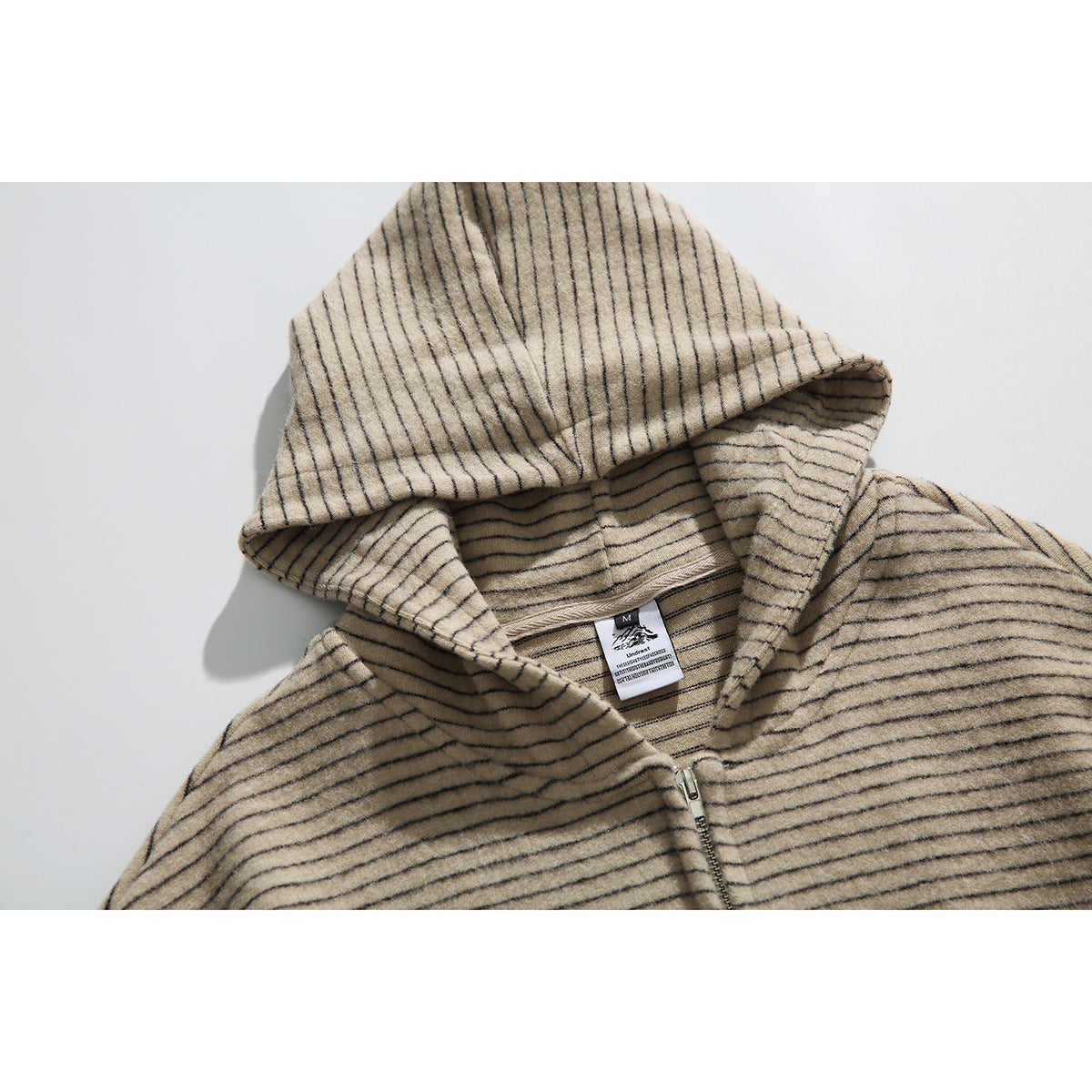 Close-up of a beige pinstriped hoodie showing its hood, neckline label, and front zipper.