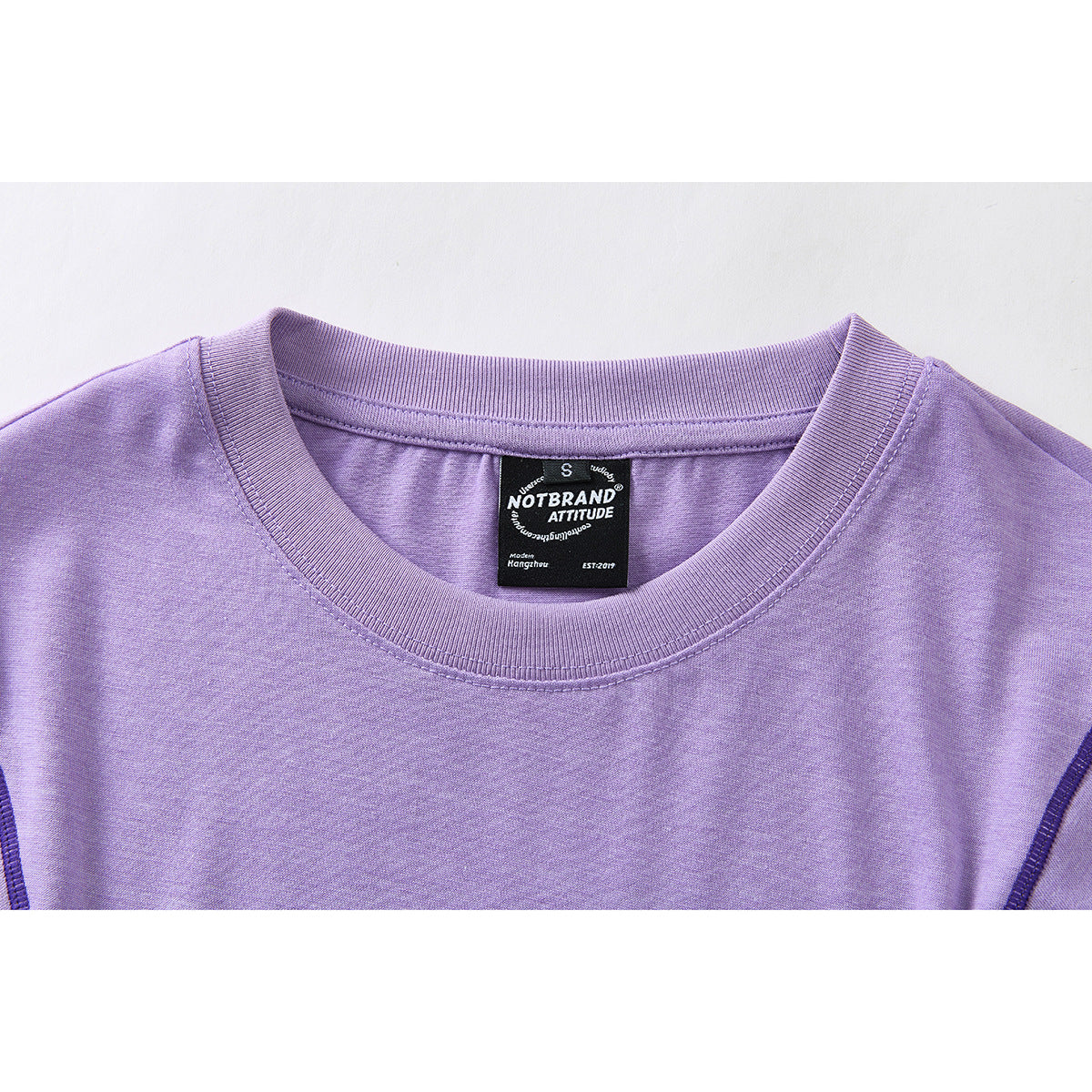 Close-up of the lavender shirt’s ribbed crew neck and black interior size and brand label.
