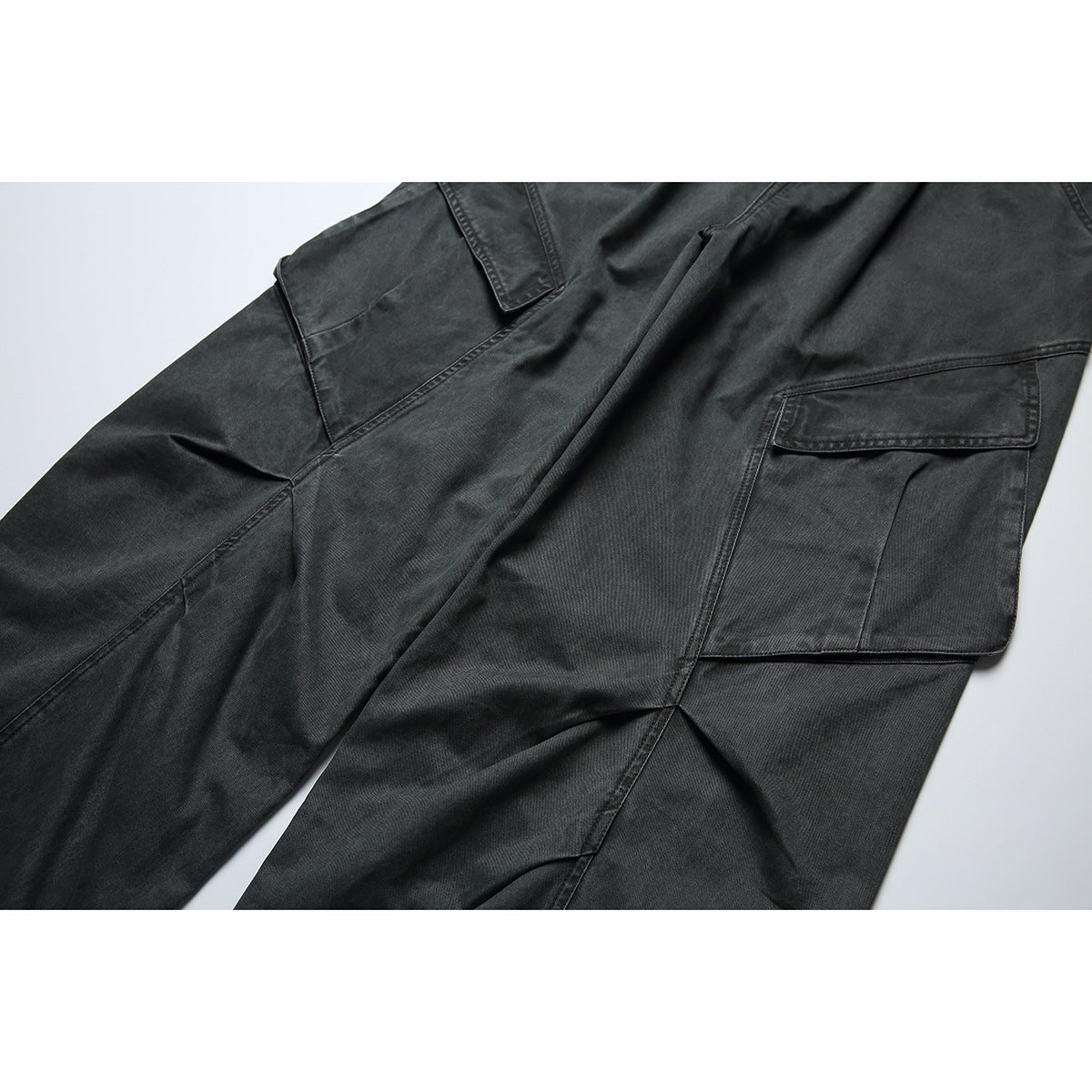 Close-up of charcoal cargo pants showing a large flap pocket and stitched panel details.