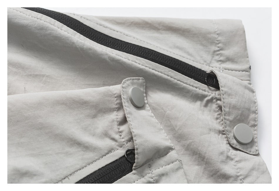 Close-up of light gray-beige pants with black zipper tracks and two pale snap fasteners.