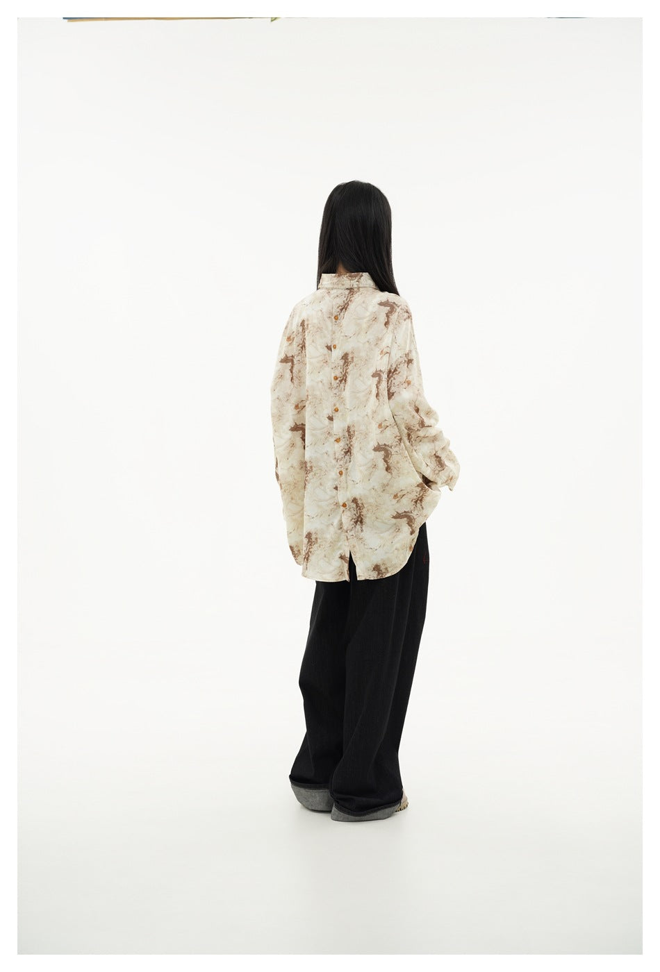 Model shown from behind wearing the cream and brown marbled shirt with loose black trousers.