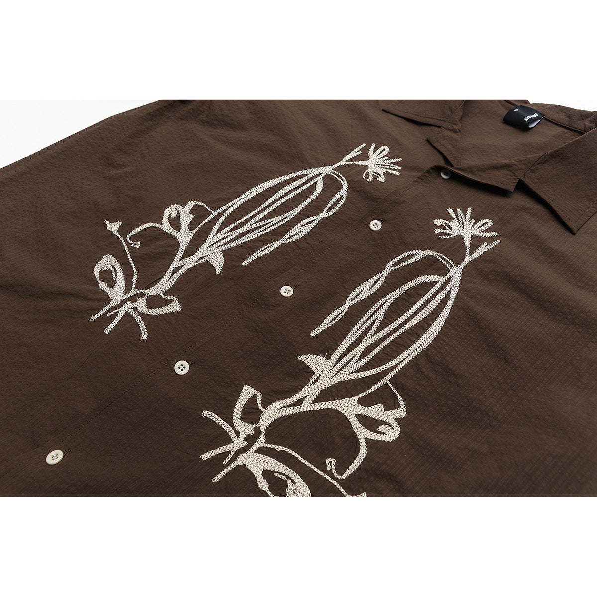 Close view of a dark brown button-up shirt with large cream embroidered bird designs across the front.