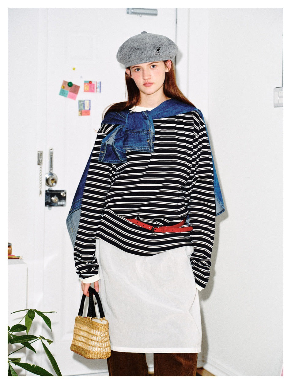 Model in navy and white striped long-sleeve top styled with denim shirt on shoulders, white skirt and small straw bag