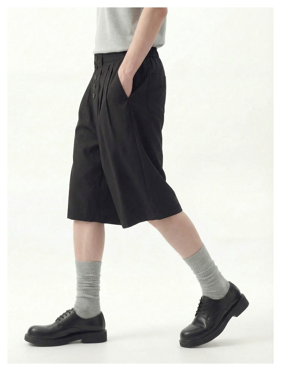 Model wearing black knee-length wide-leg shorts with a five-button front, side pockets, gray socks and black shoes.