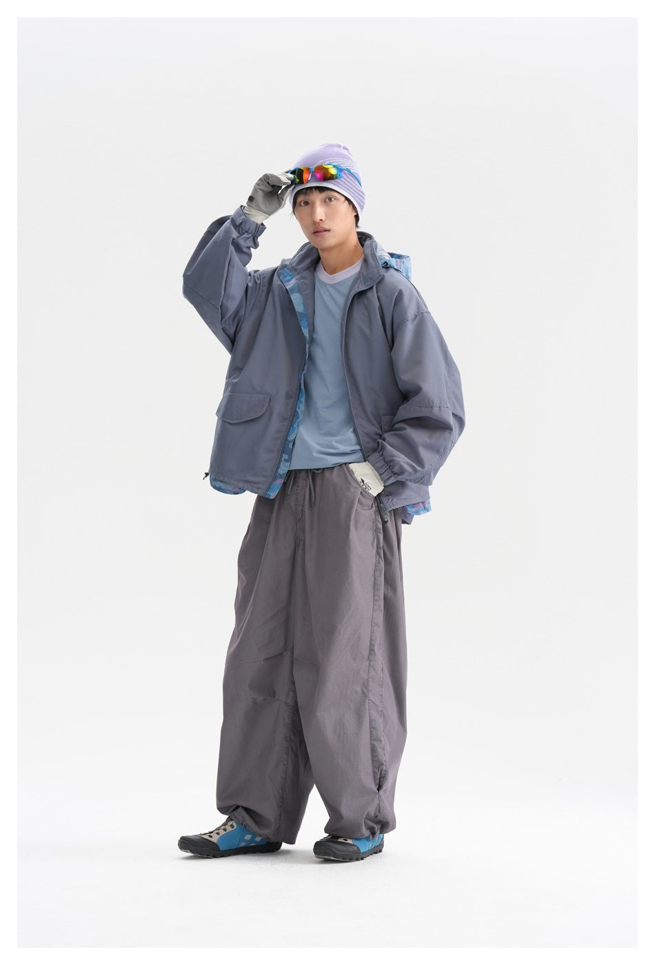 A man models a slate-gray oversized jacket with blue patterned lining, matching loose pants and a light blue shirt.