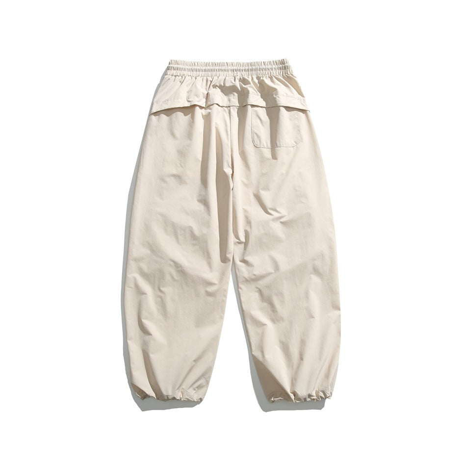 Cream relaxed-fit pants laid flat, showing an elastic waistband, rear pocket, and gathered ankle cuffs.