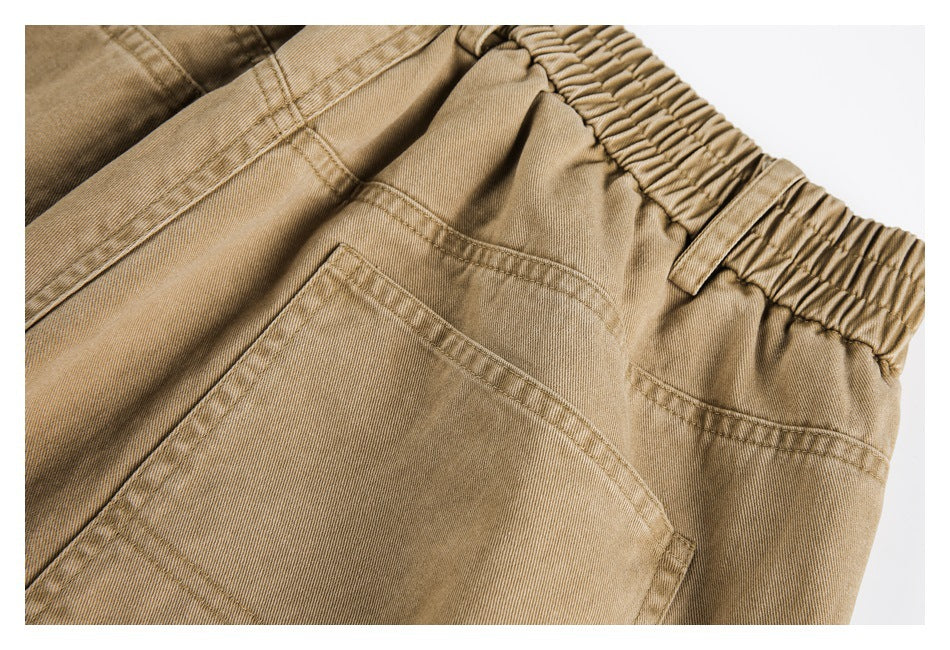 Close-up of tan pants showing an elastic waistband, belt loop, seams, and a rear patch pocket.