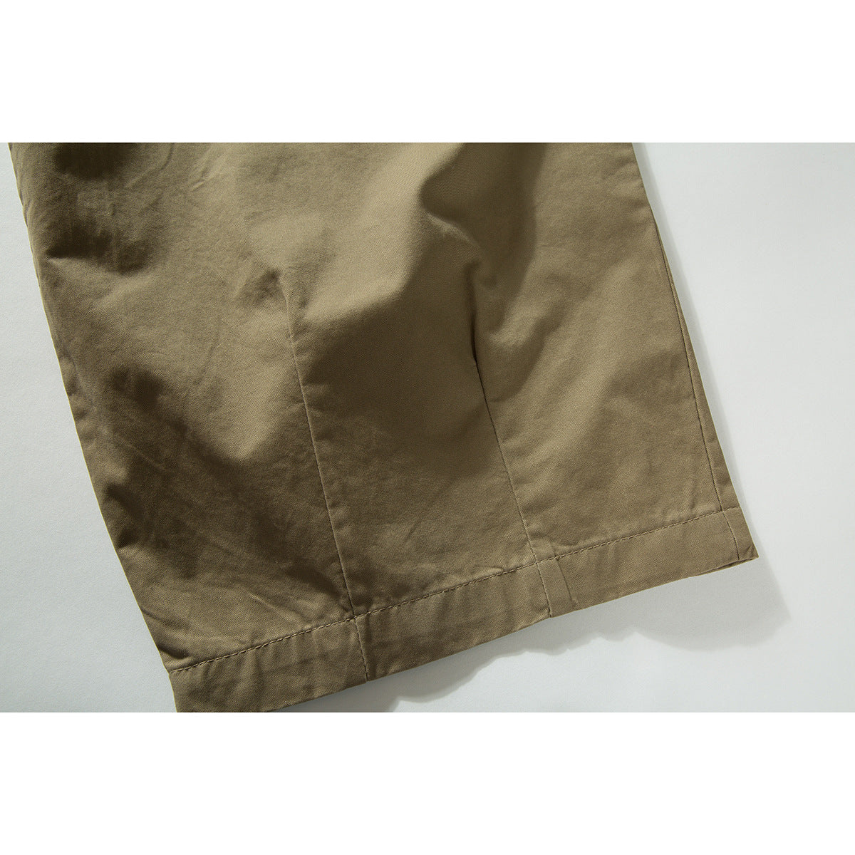 Close-up of the khaki trousers' wide leg and stitched hem.