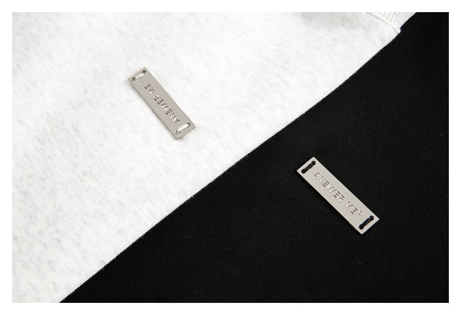 Close-up of metal ANSWER ME plaques attached to light gray and black garment fabric.