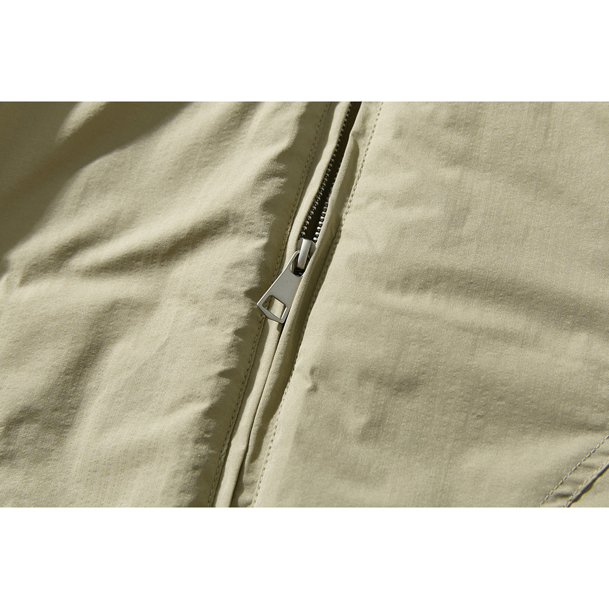 Close-up of the olive-beige jacket’s metal zipper pull and stitched front panels.