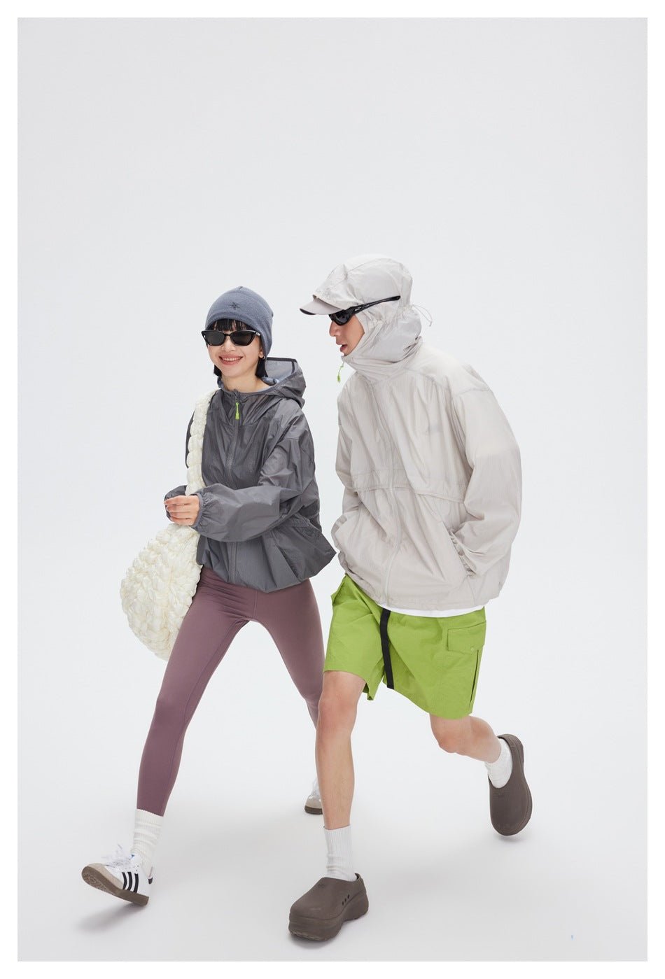 Two people walking, one in a gray hooded zip jacket and one in a pale gray jacket with the hood up