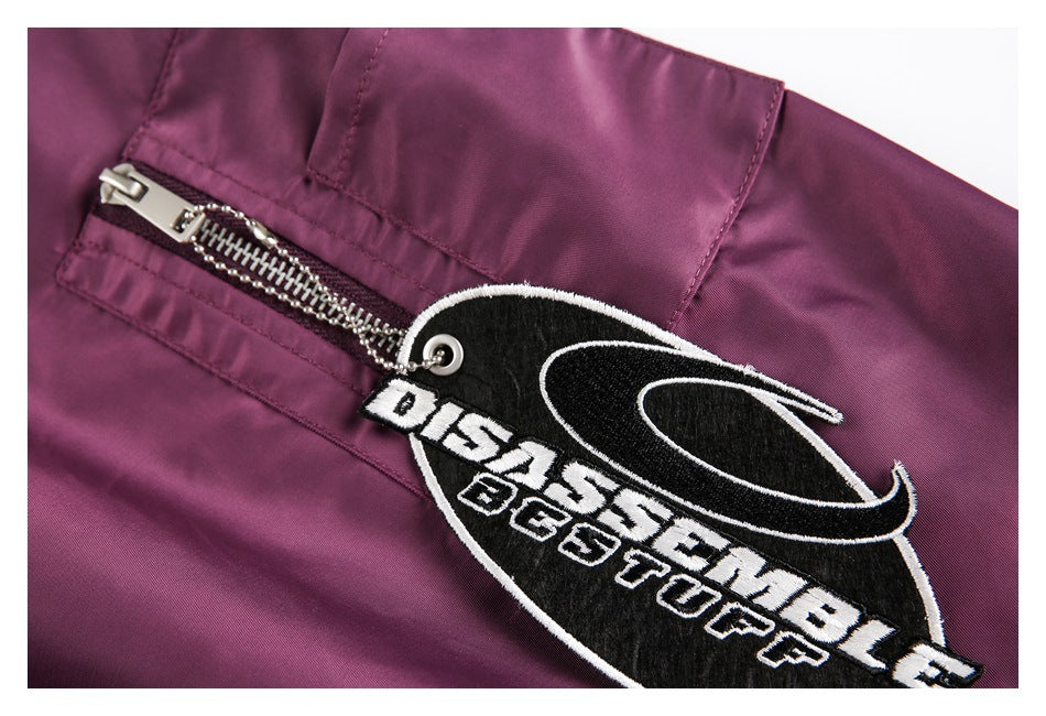 Close-up of a silver zipper and black-and-white embroidered baseball-style patch on the plum jacket.