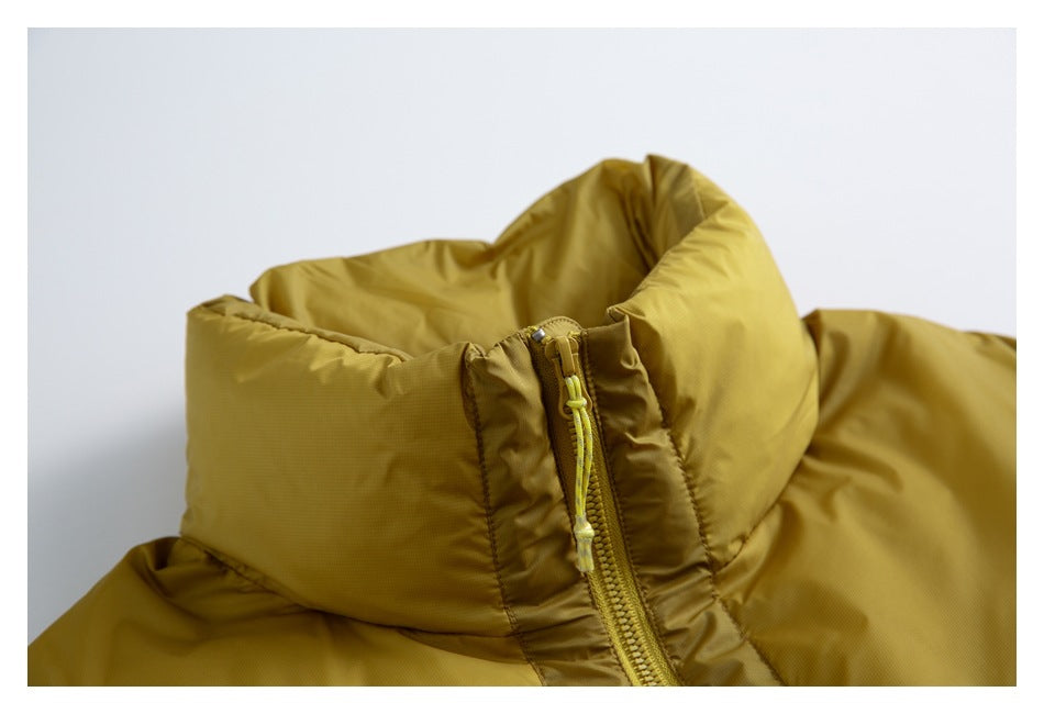 Close-up of a mustard puffer jacket's high collar and front zipper with a bright cord pull.