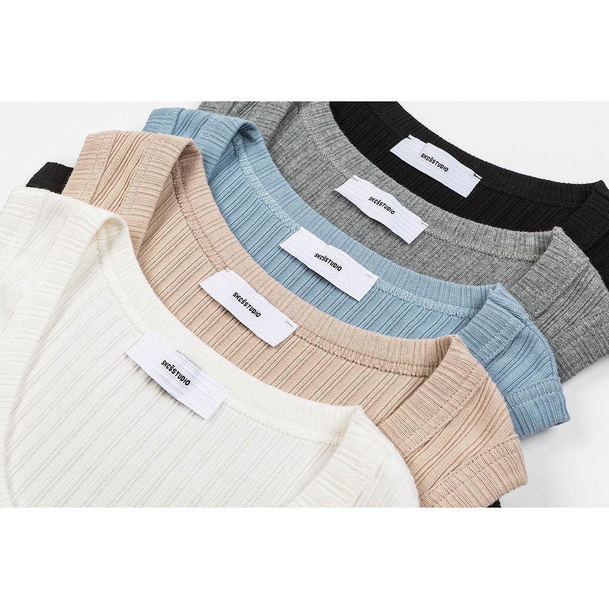 Close-up of ribbed tank tops in ivory, peach, light blue, gray, and black, with sewn neck labels.