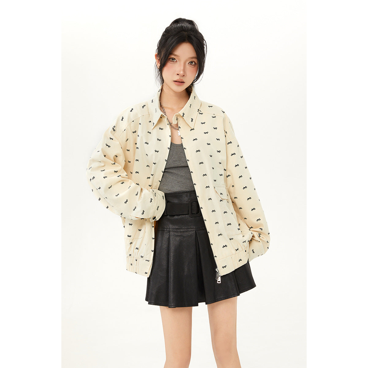 Model wearing an open cream jacket with small black bow motifs over a gray top and black skirt; front view.