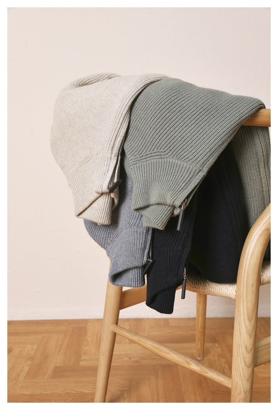 Four ribbed knit zip cardigans in beige, gray-green, gray and black draped over a wooden chair