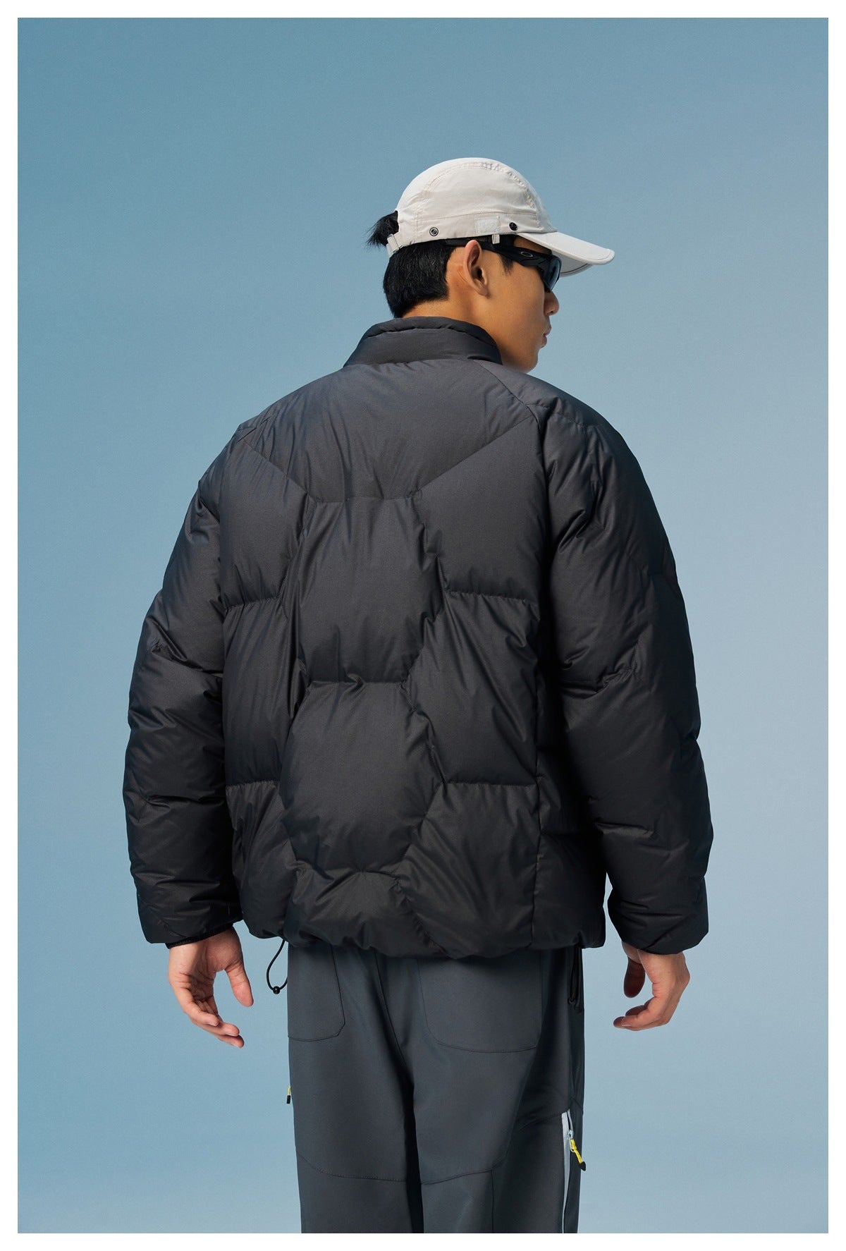 Rear view of a man wearing a black quilted puffer jacket with a high collar and dark trousers.